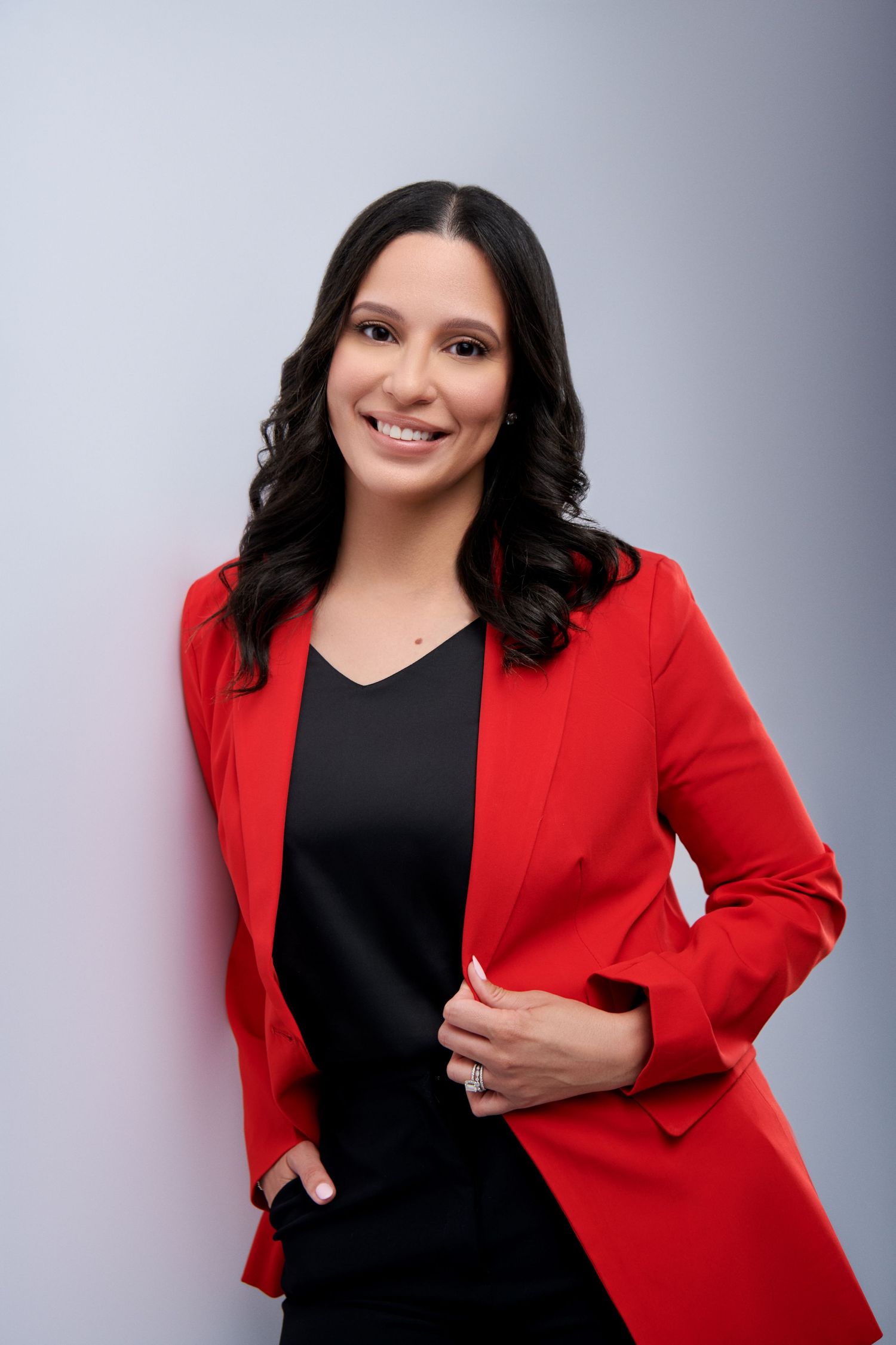 Woman in red blazer and black top smiling confidently against a light gray background.