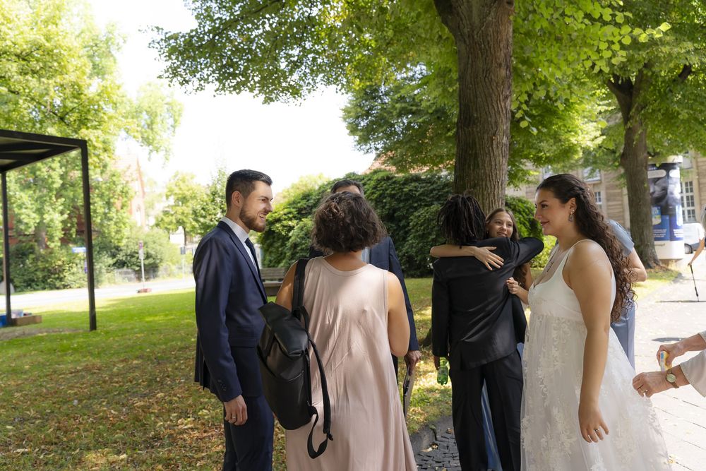 Wedding party gathering under green trees in a garden setting.