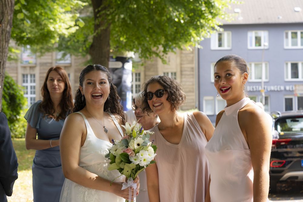 Fröhliche Braut mit Blumenstrauß lacht mit ihren Hochzeitsgästen während der Gratulation, authentische Hochzeitsreportage von Angelo Vella