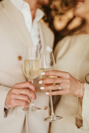 Close-up of hands holding wine glasses with engagement ring visible.