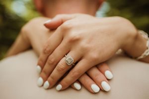 Close-up shots of hands with white nail polish and an engagement ring against cream-colored fabric.