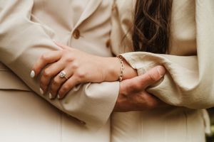 Detail shots of hands with white manicure and wedding rings against light beige clothing.