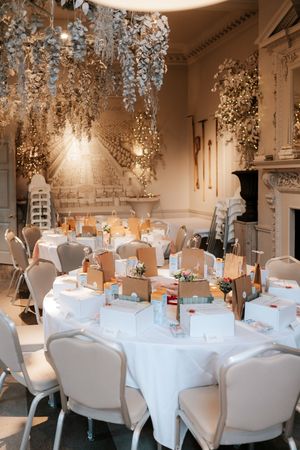 Elegant wedding reception hall with white round tables, floral ceiling installations, and warm candlelight ambiance.