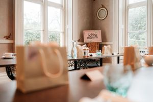 Elegant room setup for a Holding Mumma event with gift bags, water bottles, and branded signage on wooden tables.