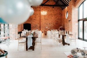 Rustic wedding venue with exposed brick walls, wooden tables, white Chiavari chairs, and elegant table settings under high ceilings.