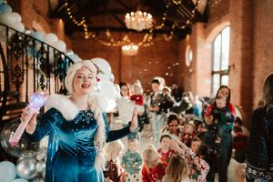 Elsa princess entertainer blowing confetti at a festive children's holiday party in a brick venue.