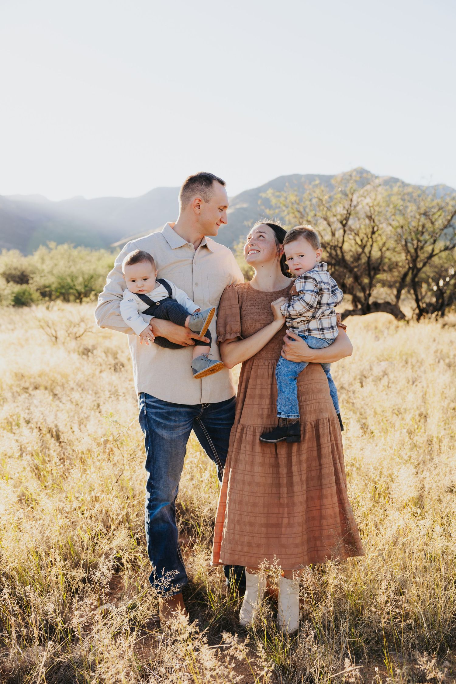 Family embracing in a golden field with mountains and desert landscape in the background.
