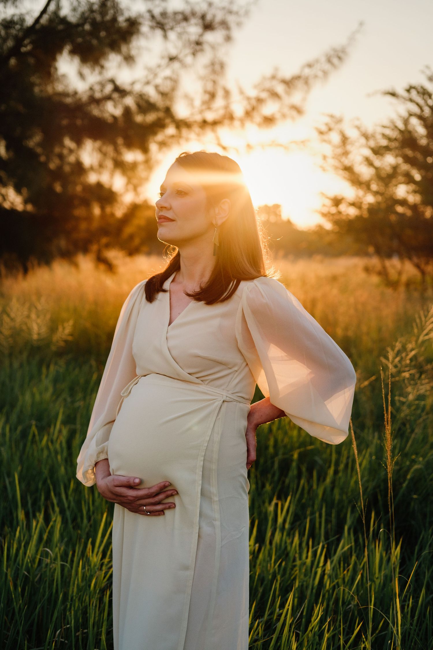 Golden hour maternity photography of an expectant mother backlit by warm sunlight in a field.