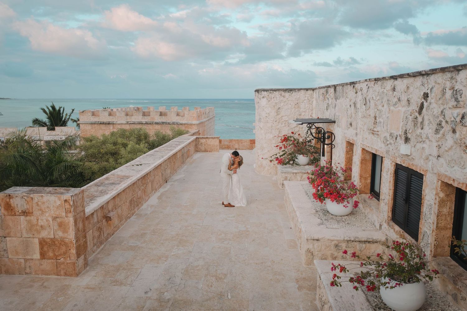 Bride stands alone on a stone terrace overlooking the ocean at a destination wedding venue.