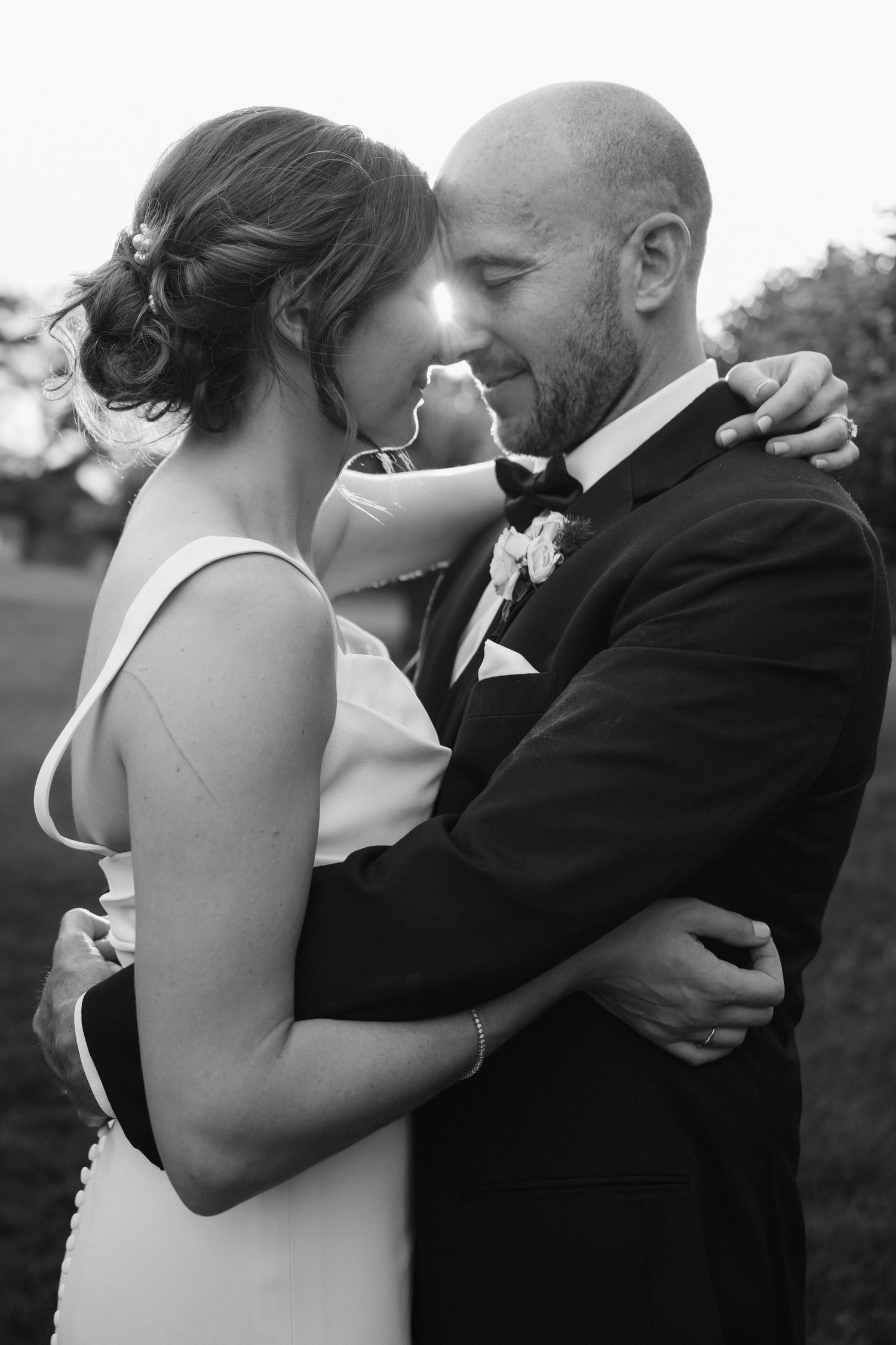 Black and white portrait of bride and groom sharing an intimate forehead touch embrace outdoors.