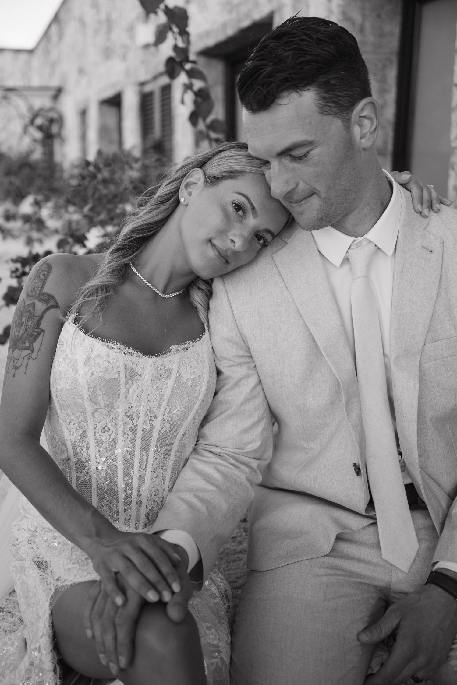 Bride rests head on groom's shoulder in an intimate black and white wedding portrait outdoors.