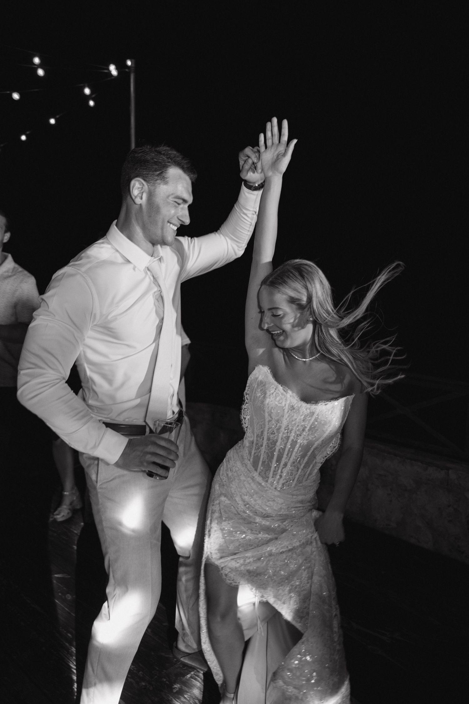 Bride and groom dance joyfully at night in a black and white wedding reception photo.