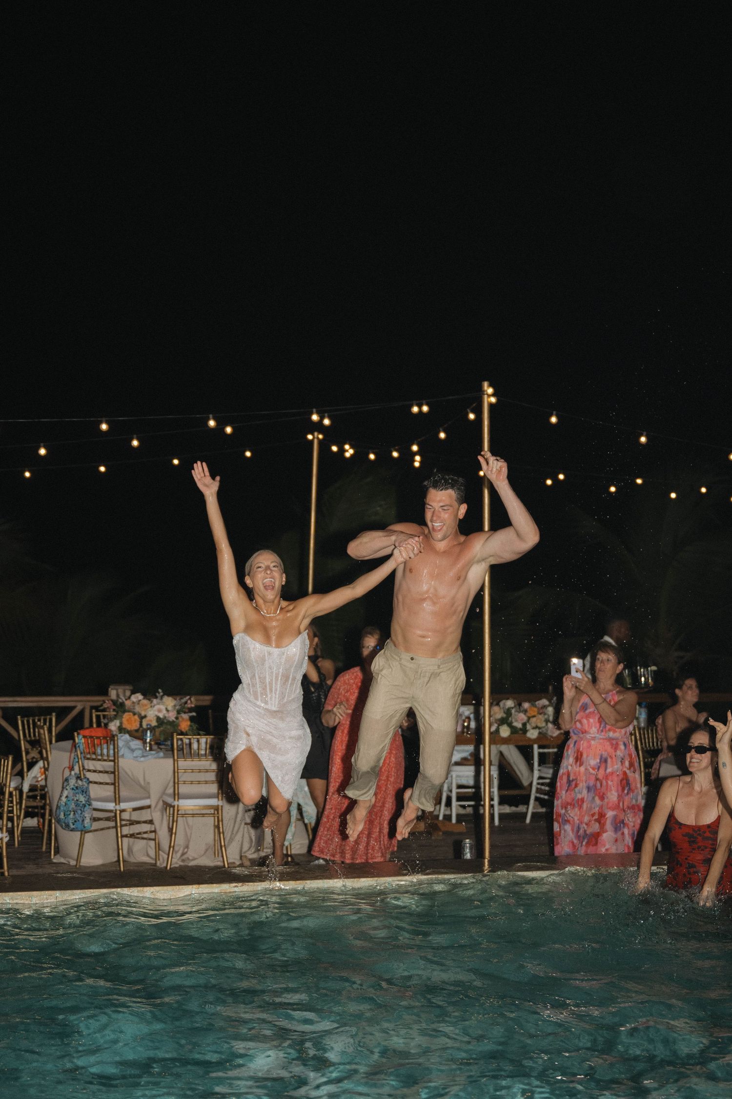 Bride and groom jump into a pool together during their festive outdoor wedding reception.