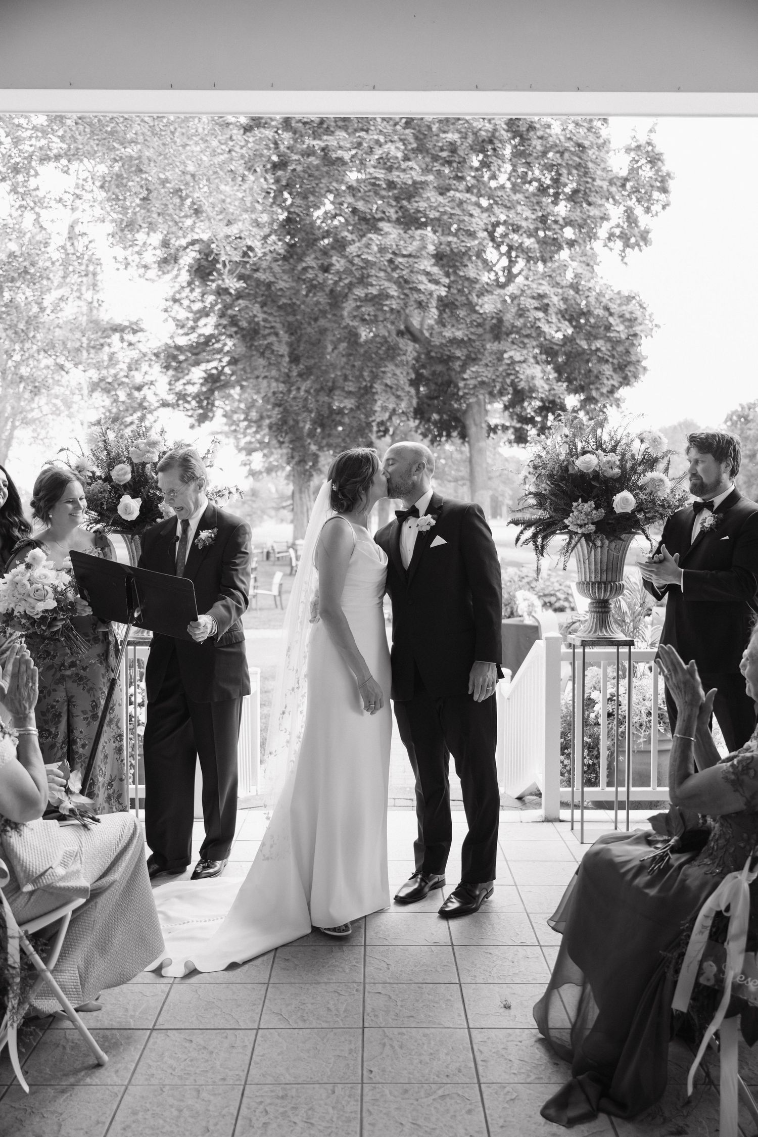 Black and white photo of bride and groom sharing their first kiss during an outdoor wedding ceremony.