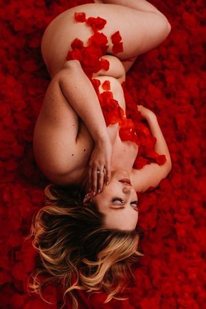 Artistic portrait on red rose petals creating vibrant contrast in intimate boudoir setting. boudoir photography in studio