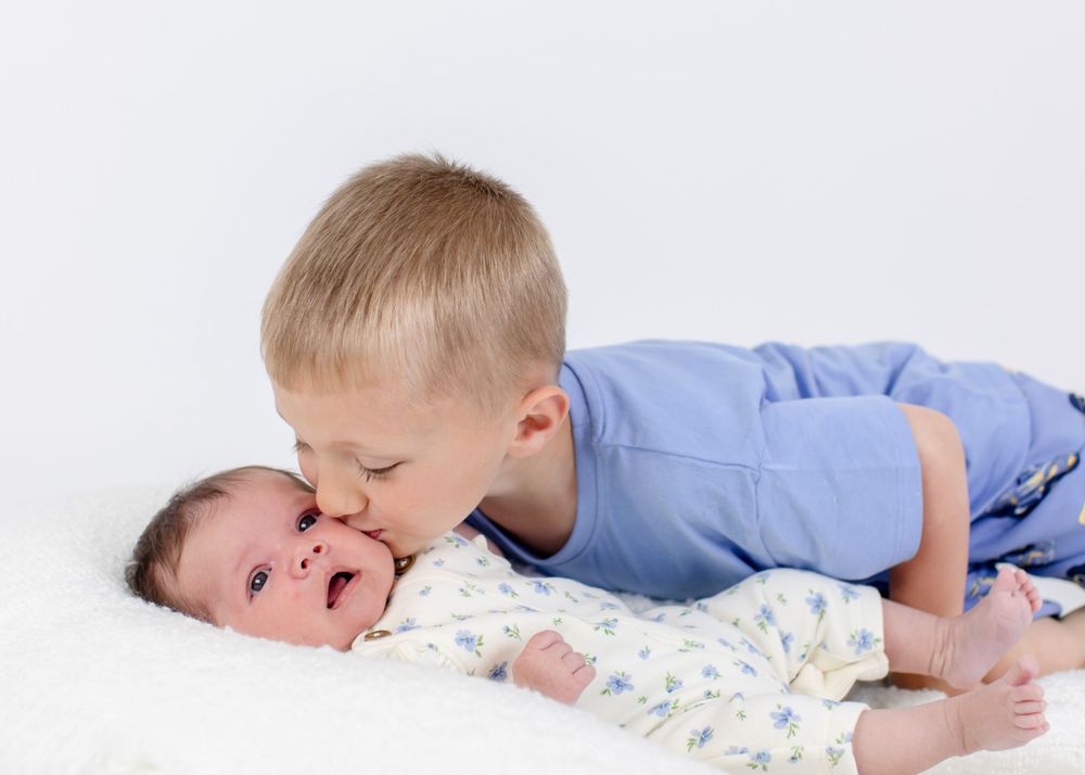Sweet candid moments of siblings playing together on white bedding.