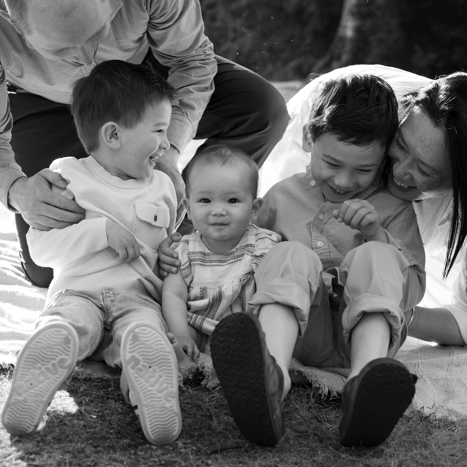 Mom, dad and three young children laughing sitting together on ground, Jericho Beach Vancouver family photographer, black and white