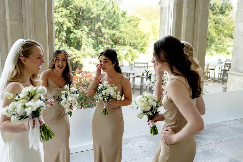 A group of bridesmaids in champagne-colored dresses share a joyful moment while holding white floral bouquets.
