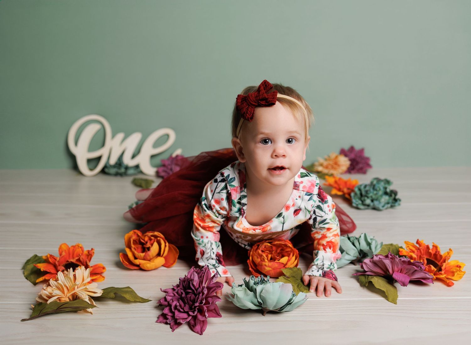 First birthday setup with floral decorations and 'one' sign against mint green backdrop.