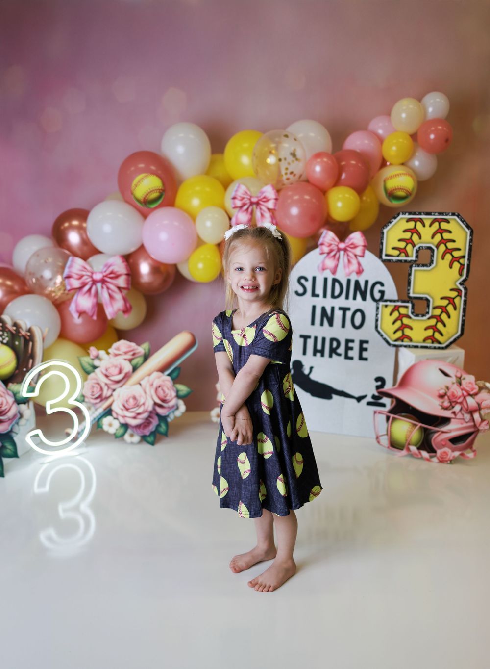 Pink and yellow balloon arch with birthday decorations and number signs for a third birthday celebration.