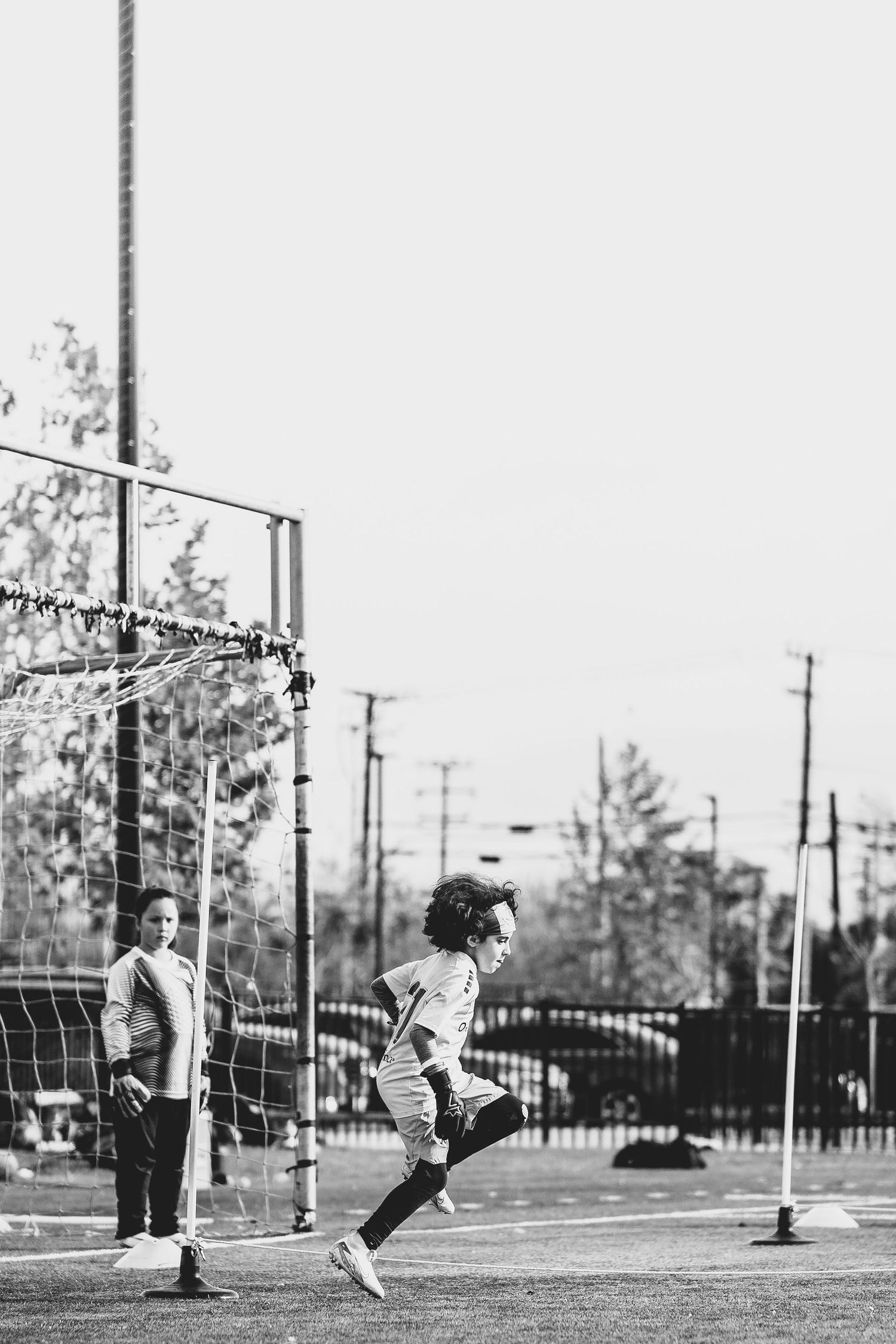 Black and white photo of soccer players practicing on field with utility poles in background.