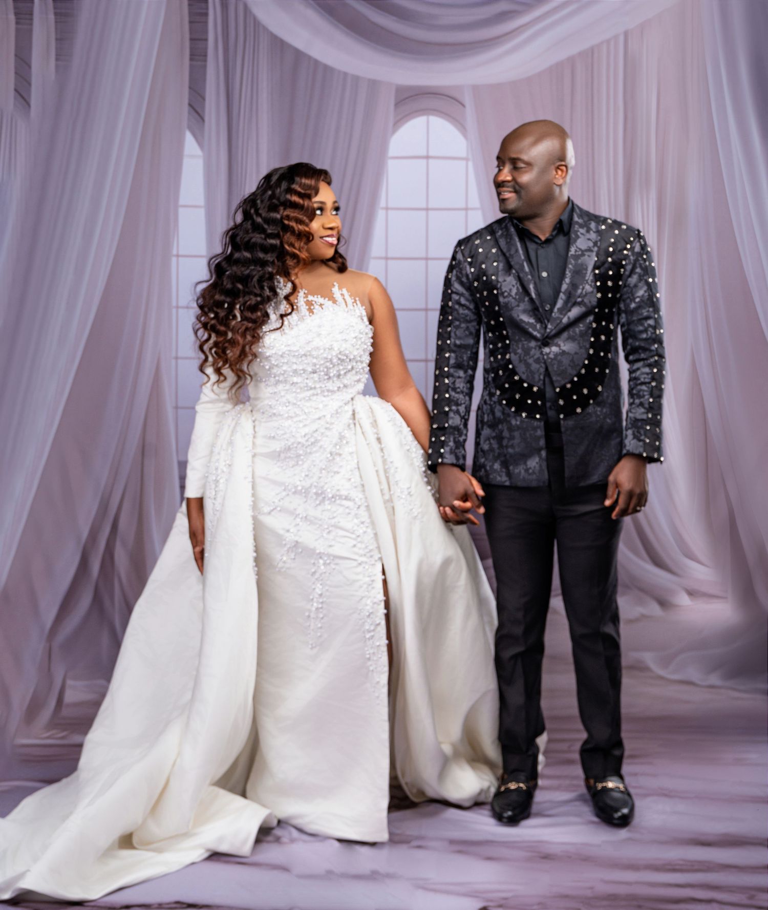 Elegant couple in formal wedding attire against white draped backdrop.