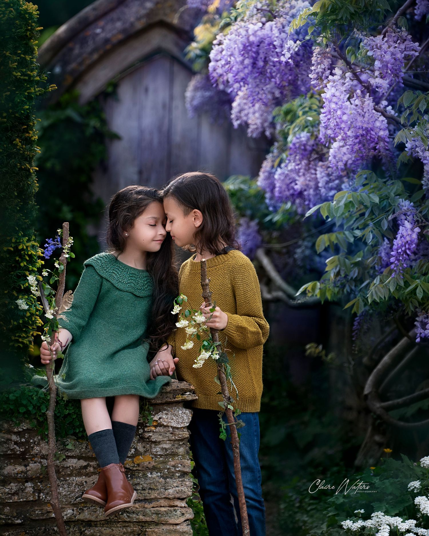 Two children sharing a tender moment under blooming purple wisteria in a magical garden setting.