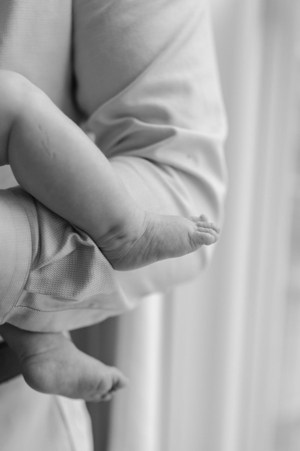 Black and white close-up of tiny newborn baby feet resting in a parent's gentle arms.