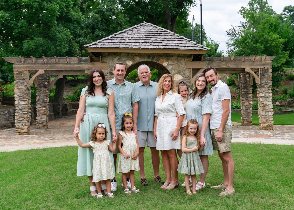 Extended family of nine posing together on a lawn in front of a stone arch gazebo in a garden.