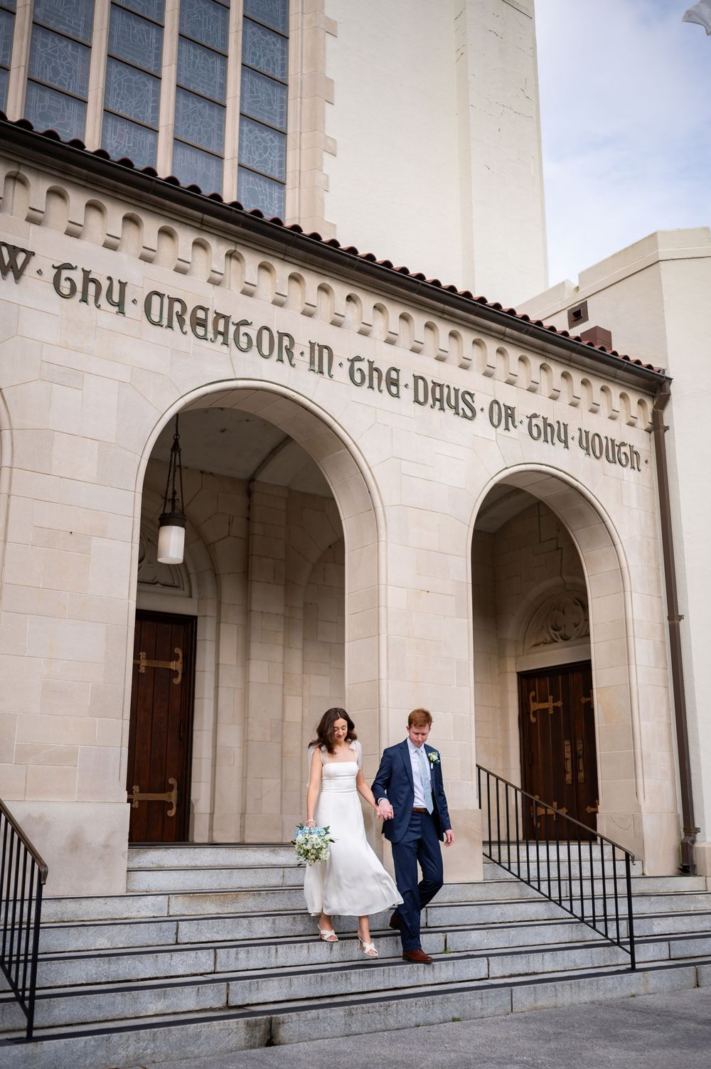 Church archways frame couple embracing in wedding attire at entrance to religious building.