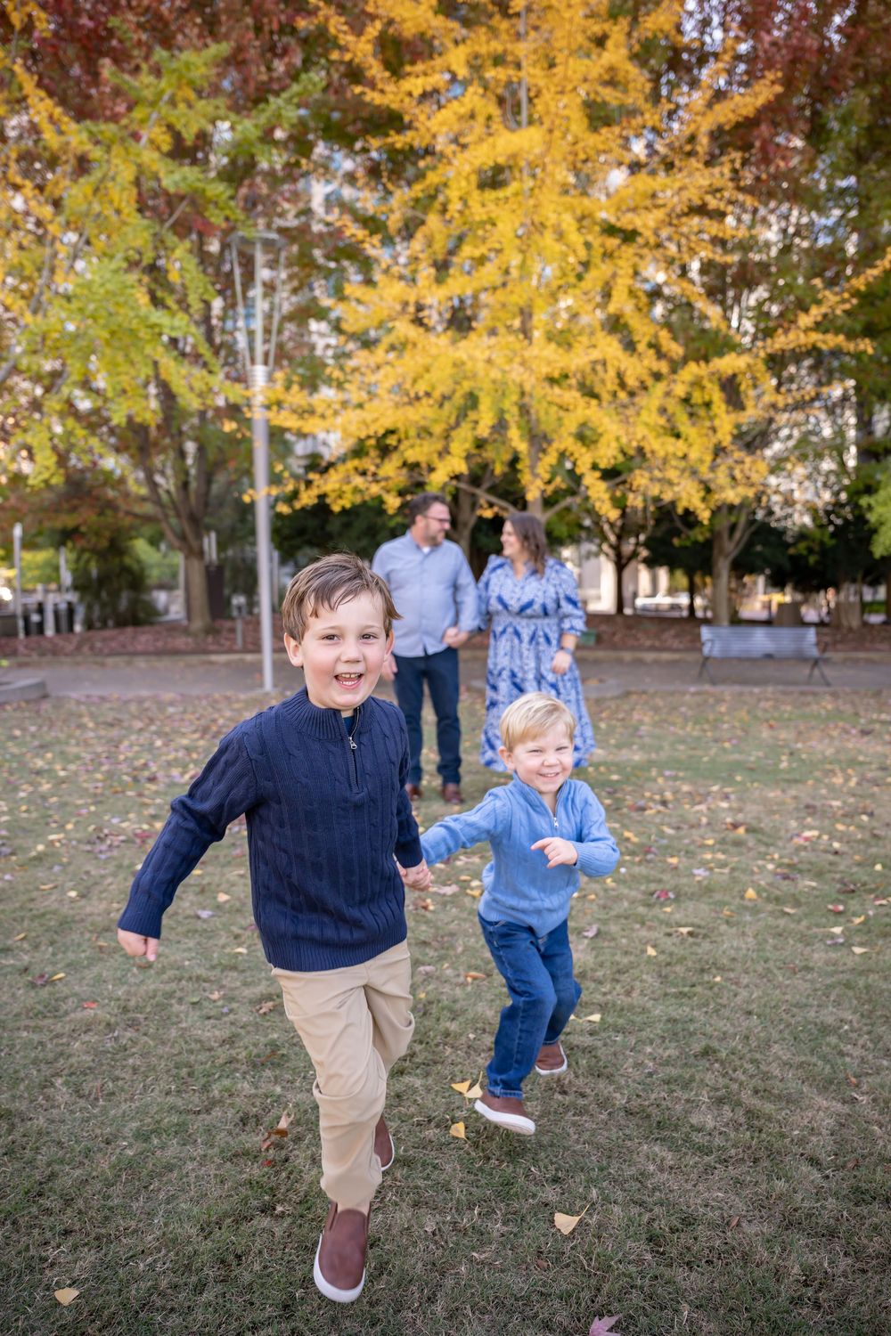 Children playing and running together on grass under golden autumn trees in a park.