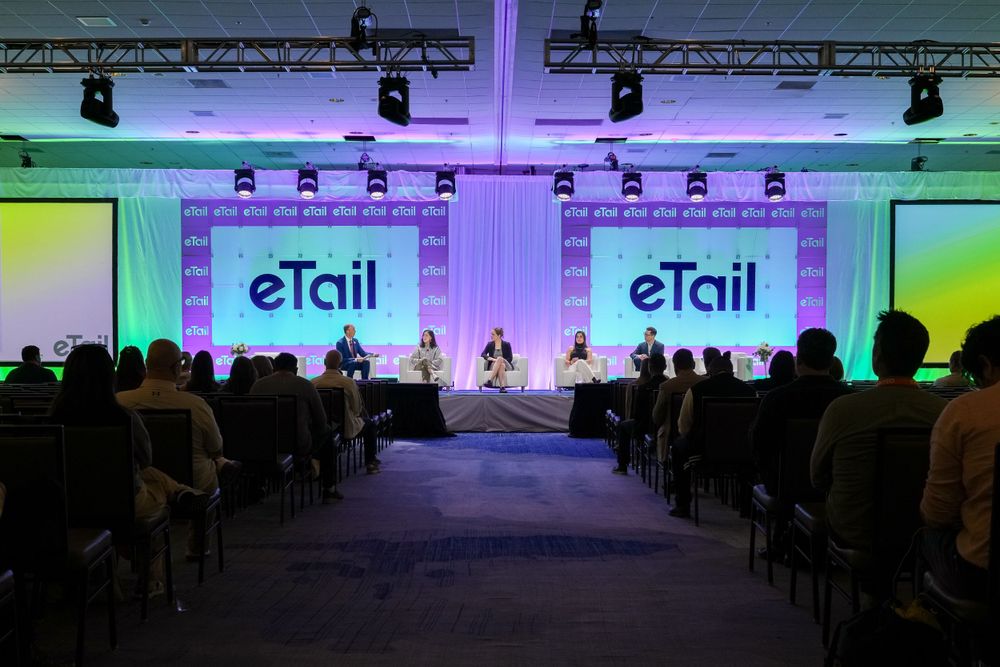 Conference hall setup with eTail branding displays and stage lighting in purple and green tones.