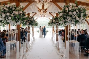 Elegant indoor wedding venue decorated with white floral arrangements and chandeliers along a light-filled aisle.
