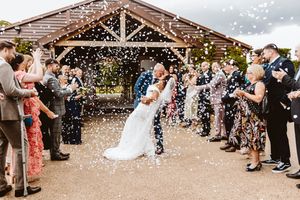 Wedding guests shower newlyweds with white confetti while forming a celebratory walkway outside.