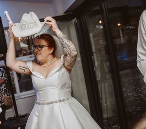 Bride in an elegant white off-shoulder wedding gown with beaded belt twirls joyfully on the dance floor.