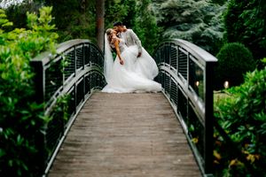A couple shares romantic moments on a wooden footbridge surrounded by lush greenery in a garden setting.