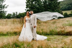Flowing white wedding veil catches the wind dramatically in a rustic outdoor field setting.