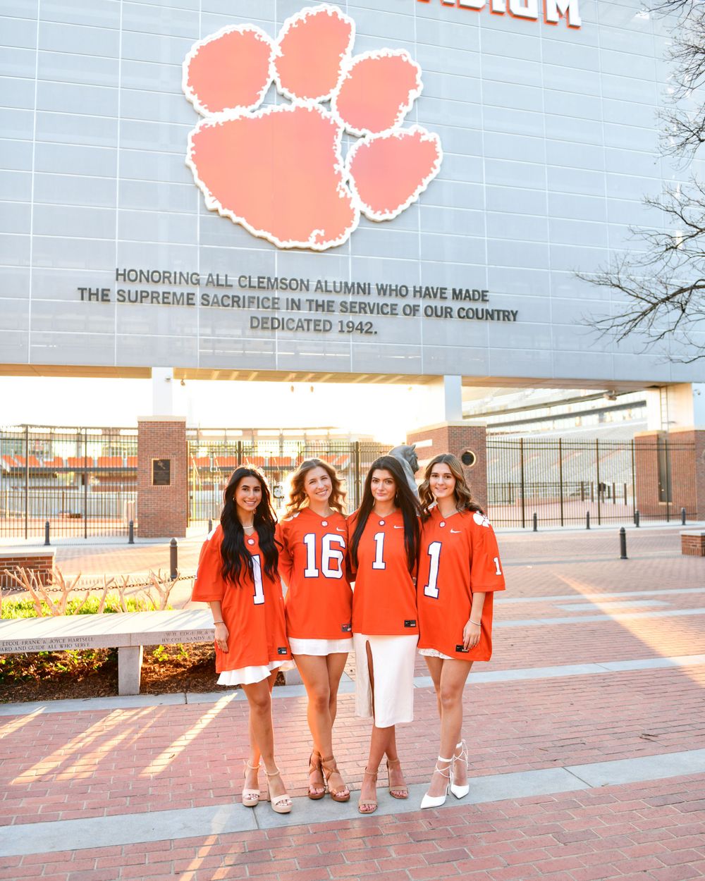 A group in orange and white outfits poses under a large Clemson paw print sign.