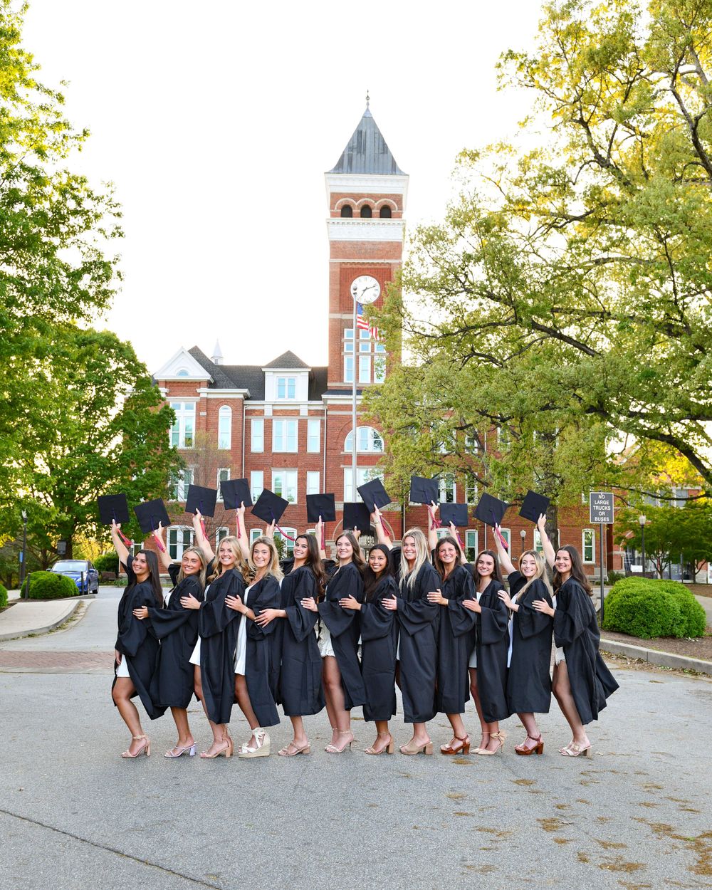 A group in graduation caps and gowns poses together in front of a brick clock tower.
