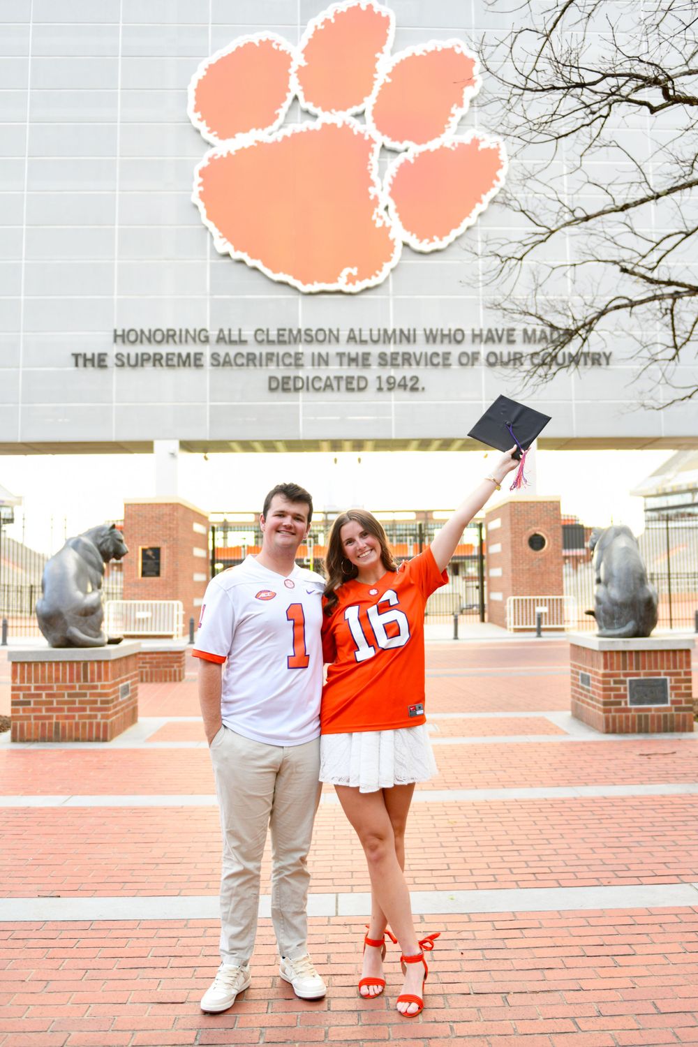 Two graduates pose in front of the Clemson University tiger paw memorial wall during graduation celebrations.
