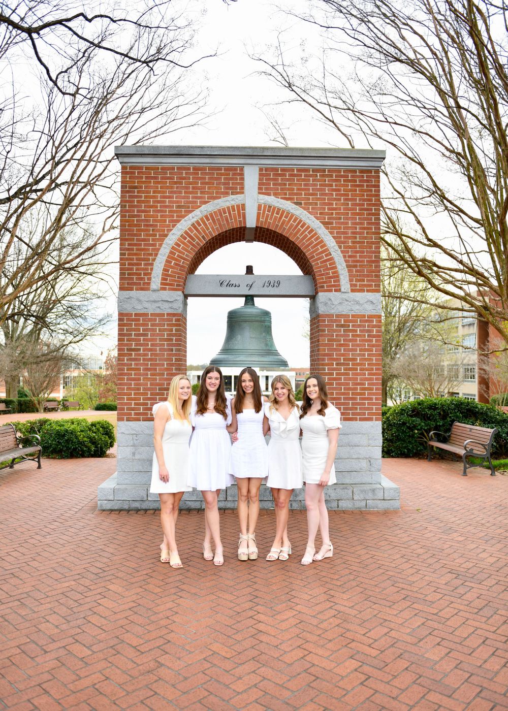 Five people in white dresses stand under the historic bell tower arch at Clemson University.