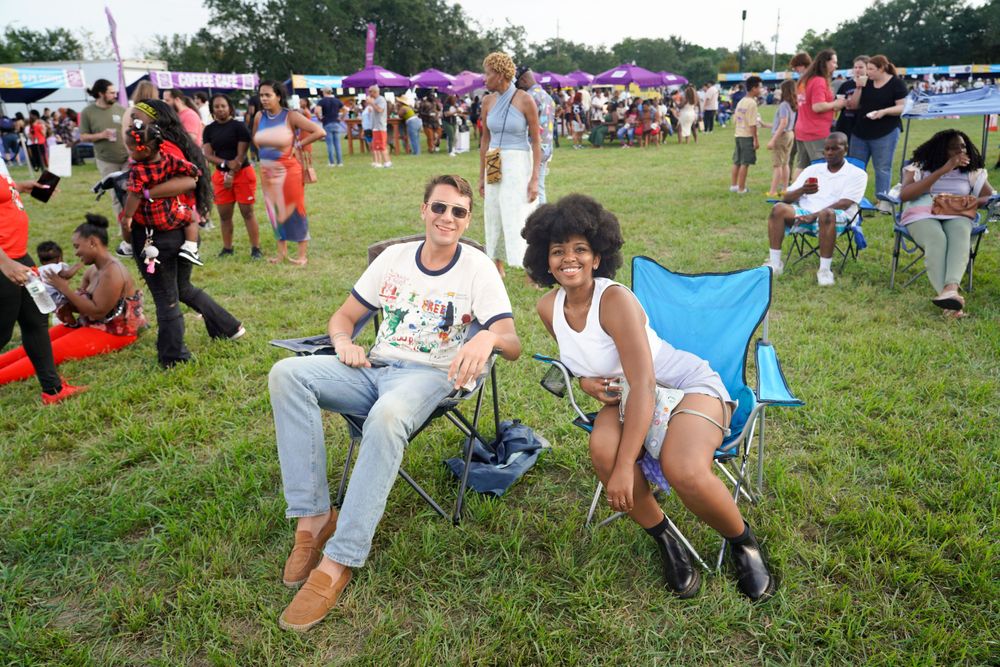 Festival attendees relax in camping chairs on grassy field during outdoor event.