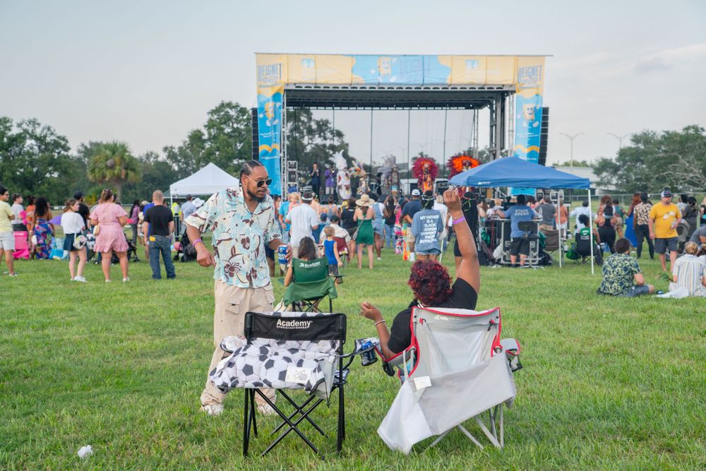 People watch performance from lawn chairs in front of outdoor festival stage.