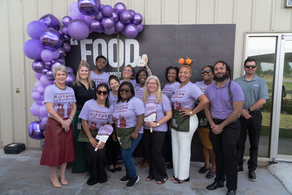 Group of staff members pose together under purple balloon arch with FOOD sign.