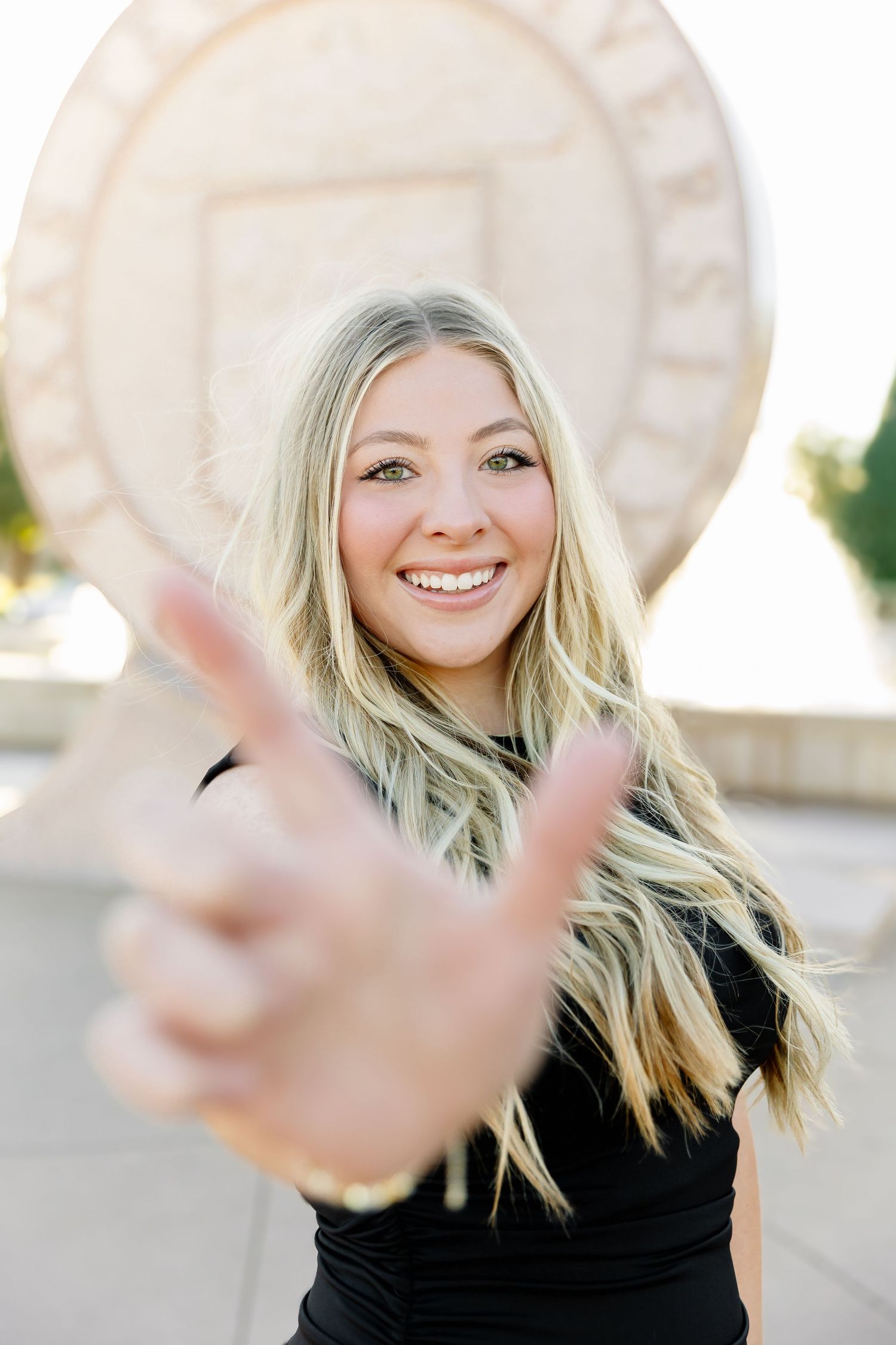 A person in black making a peace sign gesture against a light architectural background.