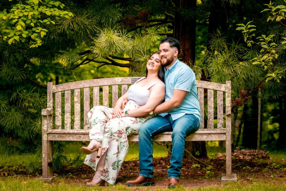 A romantic couple sitting together on a wooden bench in a lush garden setting during summer.
