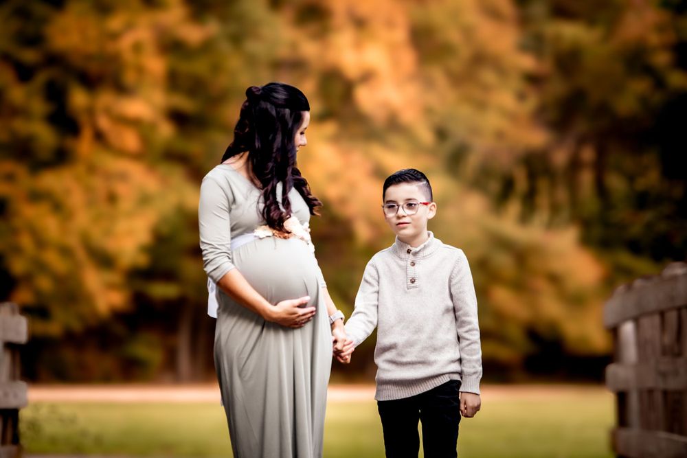 Maternity photo of pregnant woman in grey dress with young boy in autumn setting.
