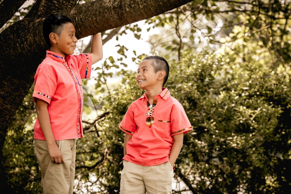 Two children in matching coral shirts share a fun moment together outdoors under dappled sunlight.