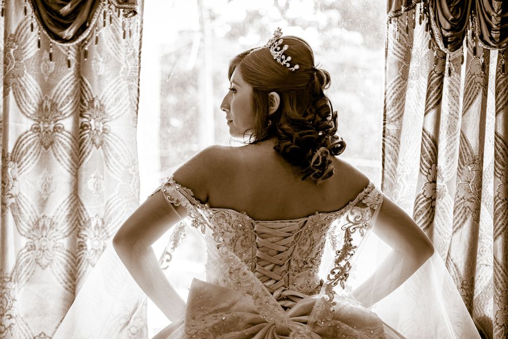 Bride in elegant lace wedding gown with corset back and tiara, posed gracefully in sepia-toned portrait.