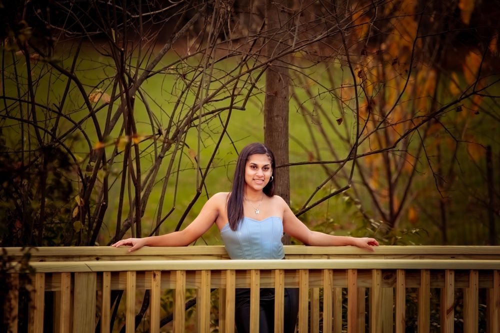 Person in a light blue tank top leaning on wooden railing with autumn forest backdrop in soft golden light.